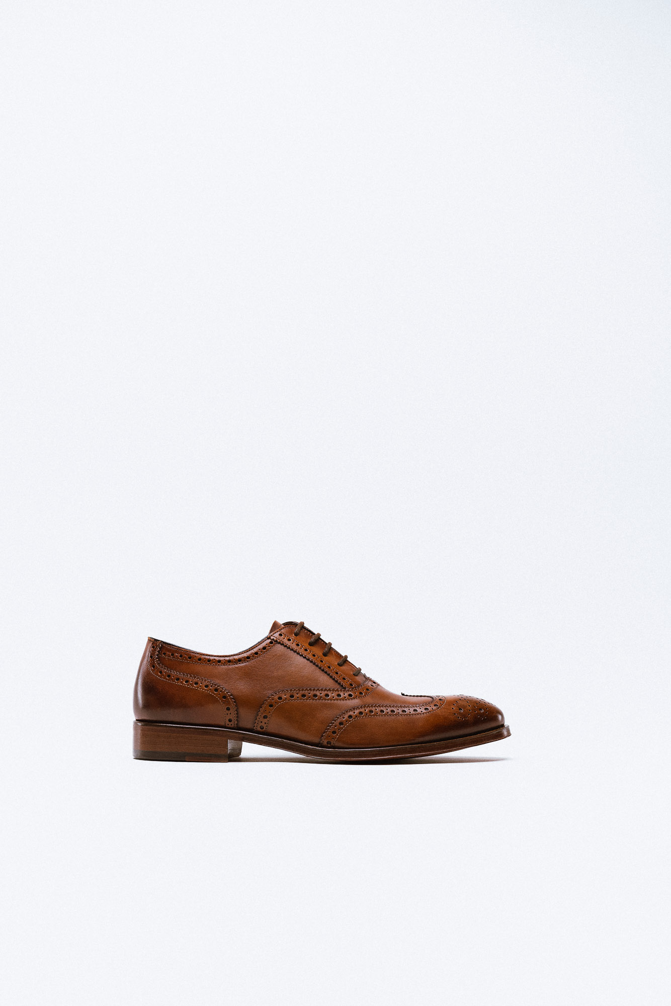 A tan leather wingtip oxford with brogue detailing and wooden heel.