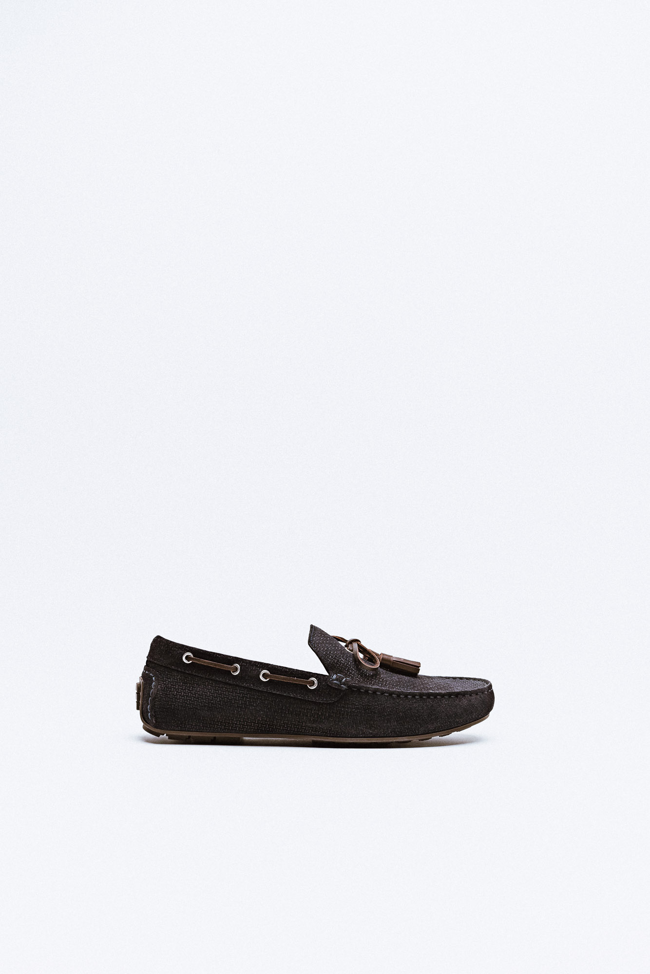 A dark brown suede driving moccasin with tassel detail and contrast stitching.