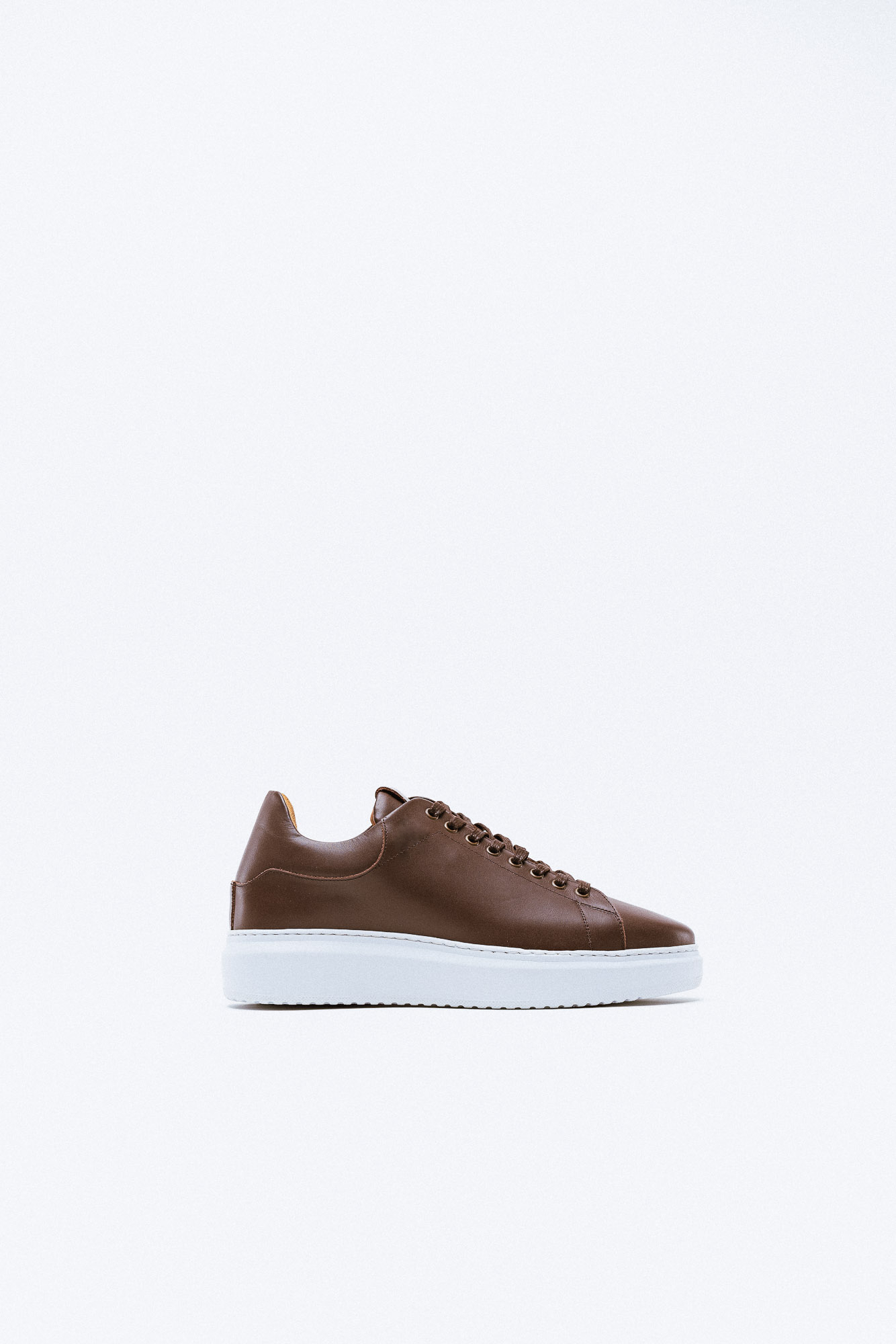 A brown leather sneaker with white platform sole and minimalist design.