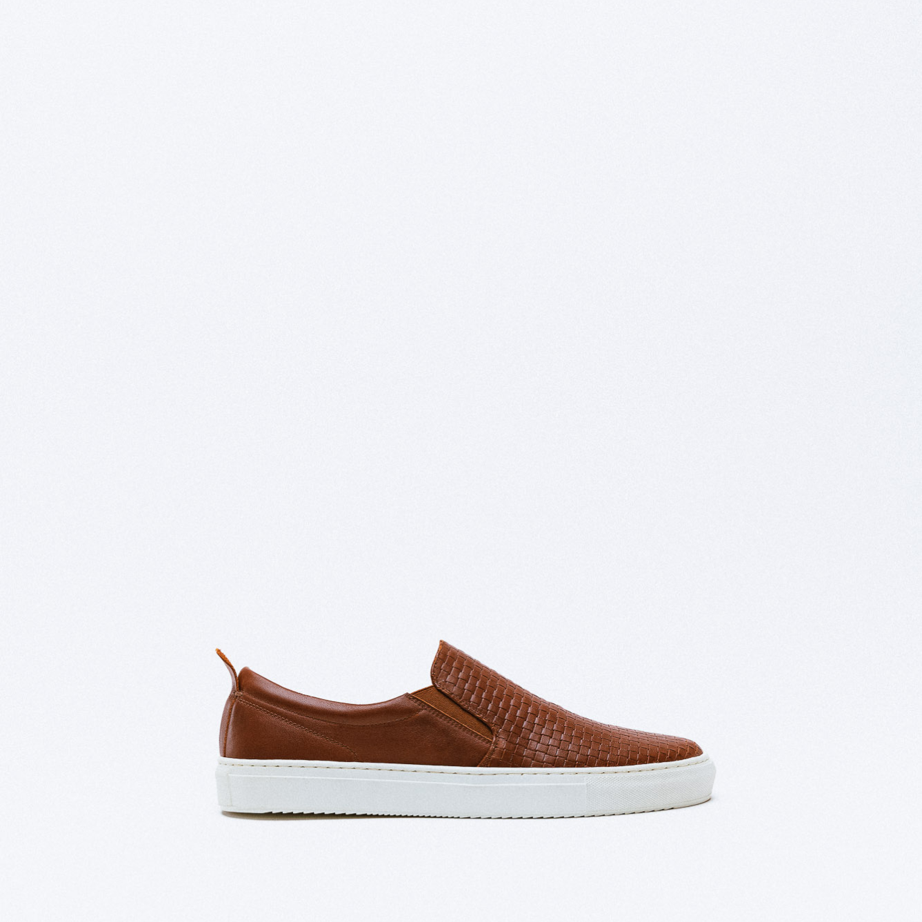 A brown leather slip-on sneaker with woven leather detail and white rubber sole.