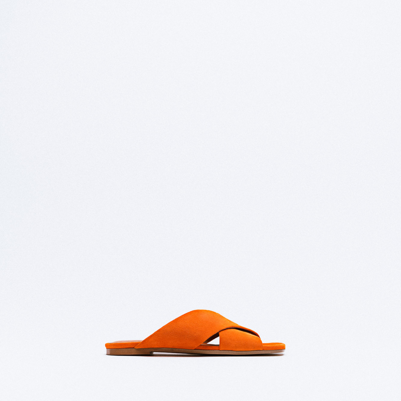 A bright orange suede sandal with crossed straps and a flat leather sole.
