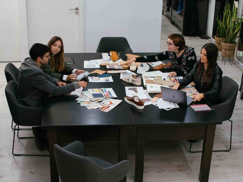 Portugal Shoes team meeting around a table full of different materials, shoe components, discussing a shoe collection.