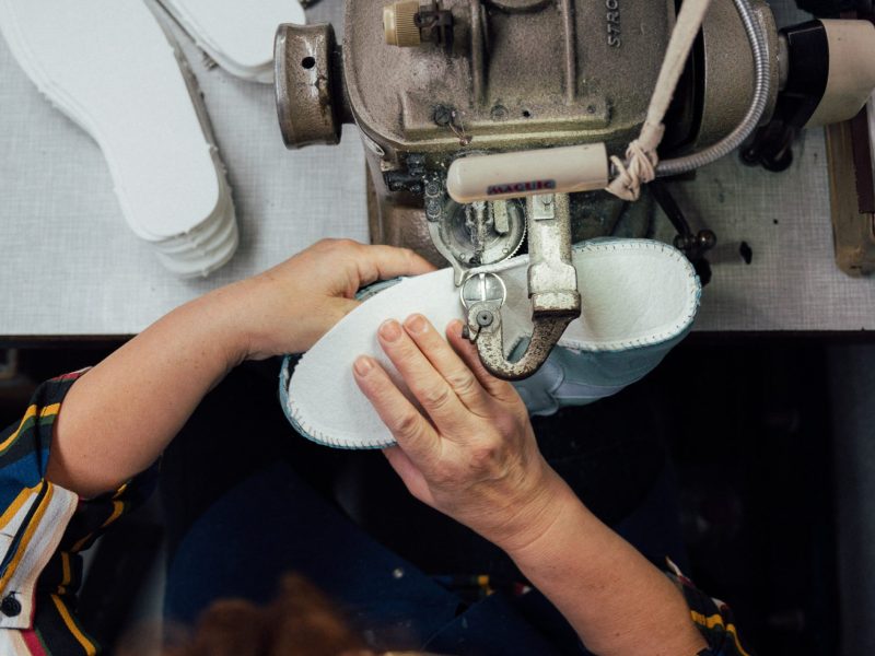 Factory worker sewing a shoe in a machine.